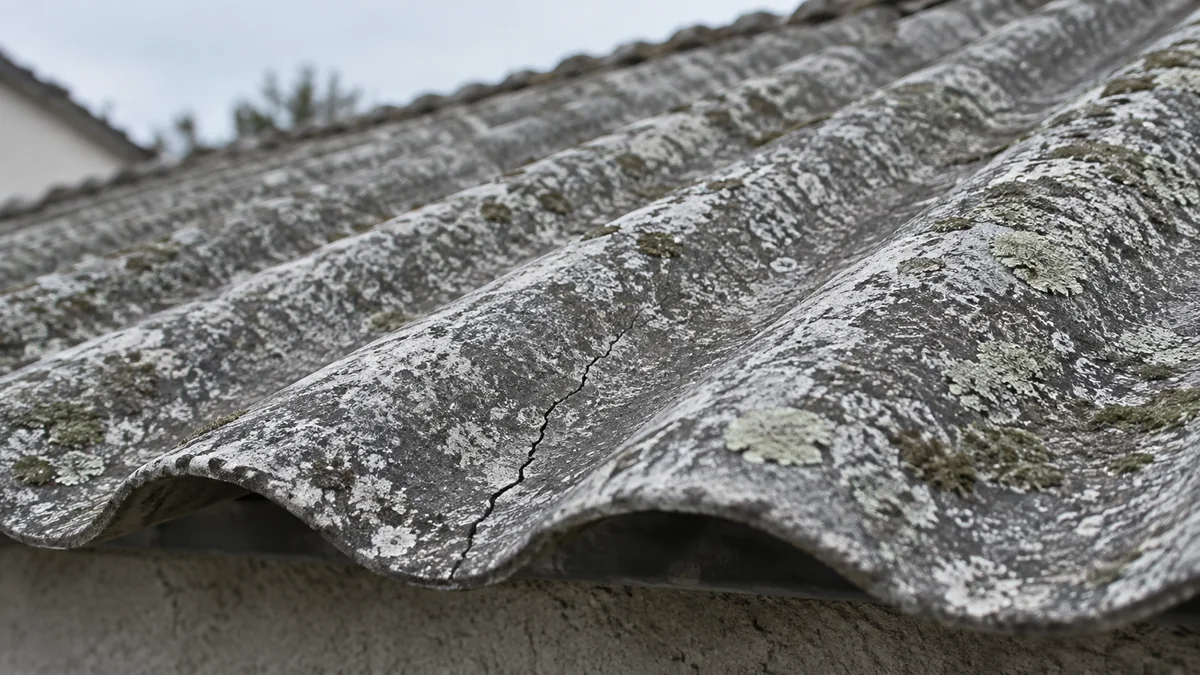 Gros plan sur une ancienne plaque de toiture ondulée en fibro-ciment, fissurée et patinée par les intempéries