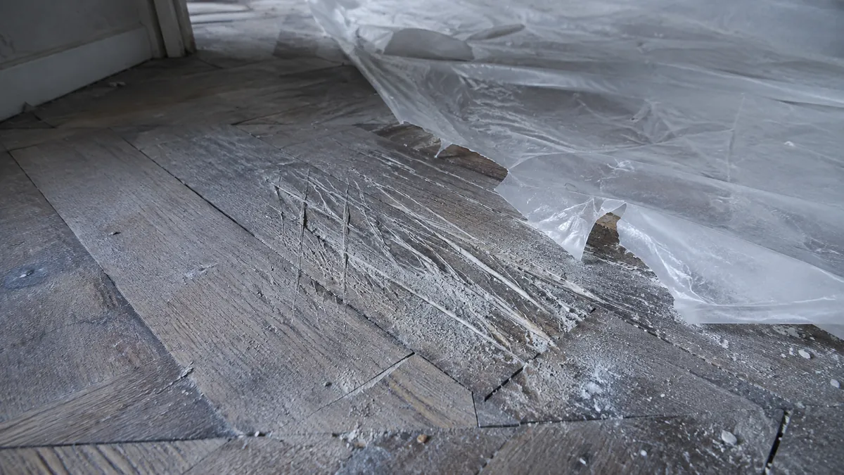 Parquet ancien profondément rayé au ras d'une bâche de protection déchirée, poussière de plâtre incrustée