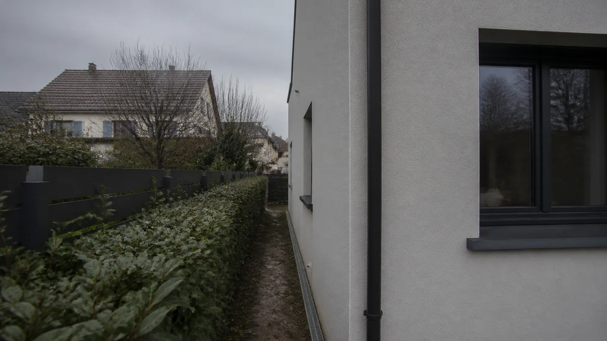 Géomètre-expert utilisant une station totale sur trépied pour vérifier l'implantation d'une maison en construction