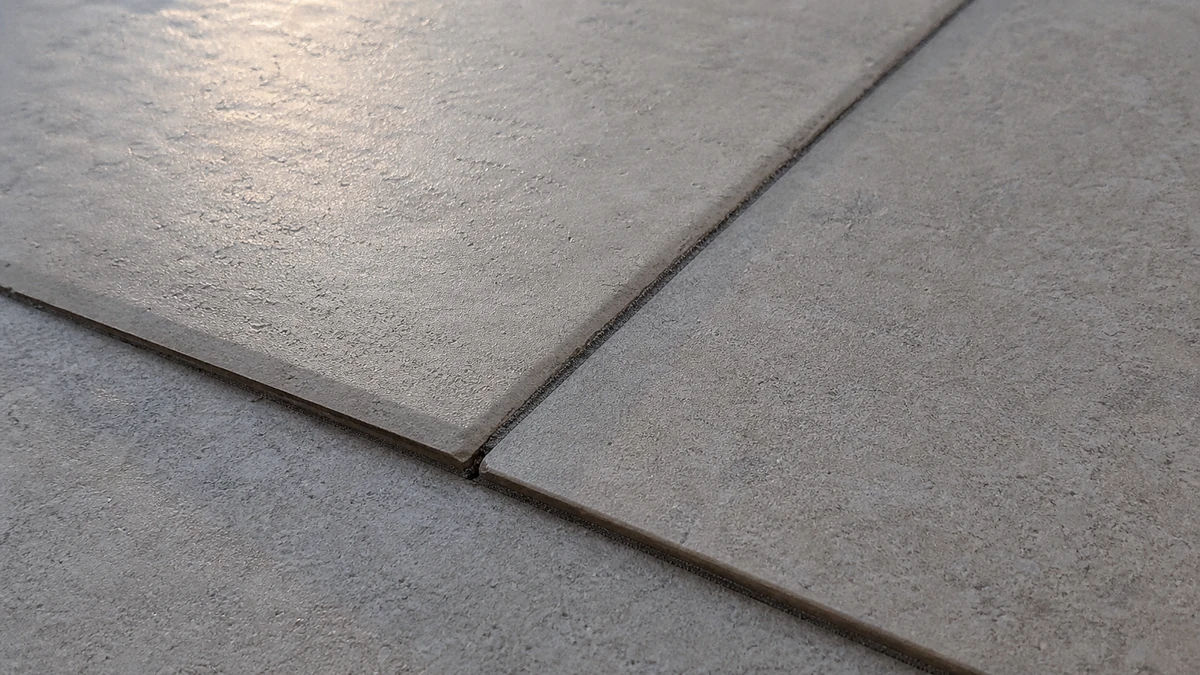 Carrelage de sol désaffleuré avec un joint irrégulier, lumière rasante accentuant le défaut de pose, sans aucune personne visible