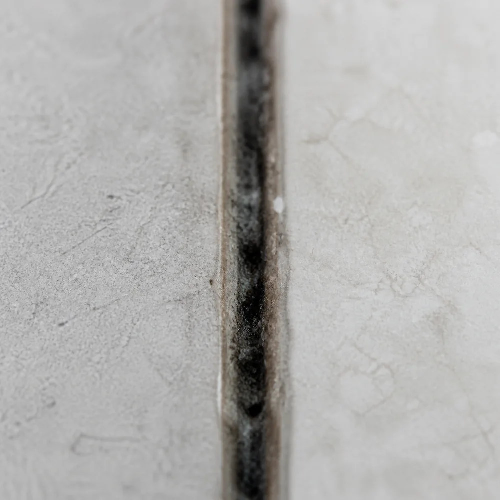 Gros plan sur un joint de carrelage noirci au pied d'une douche, avec des traces d'humidité entre les carreaux