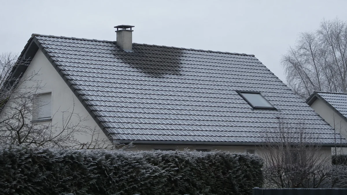 Toiture en tuiles couverte de givre par matin d'hiver, avec une zone irrégulière de tuiles sans givre révélant une déperdition de chaleur