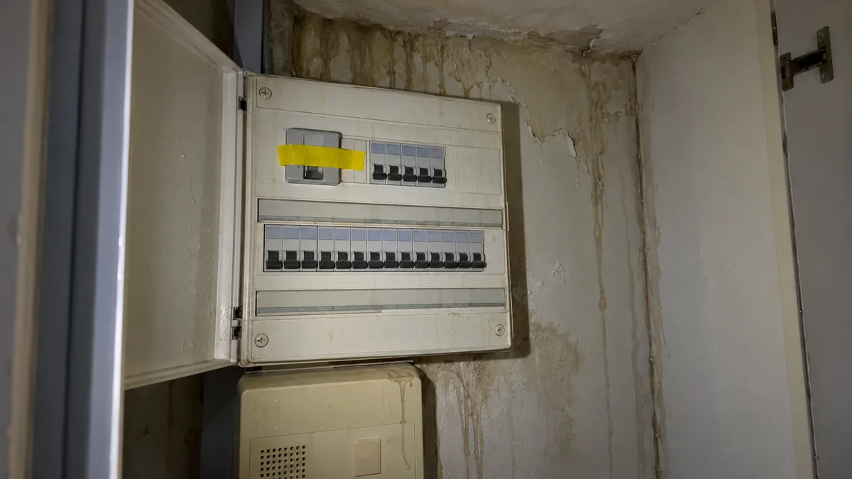 Tableau électrique d'un appartement après un dégât des eaux : disjoncteurs abaissés, ruban adhésif sur l'interrupteur général, coulures d'eau brunâtres sur le mur autour