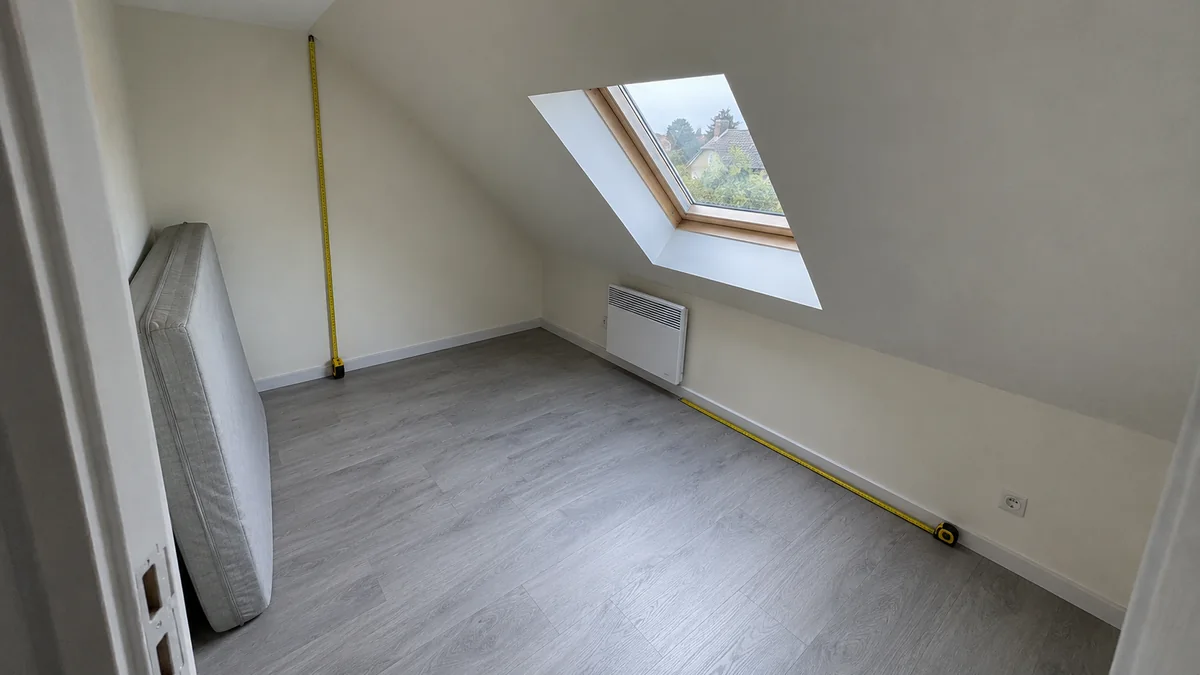 Studio sous les combles d'une maison divisée, avec deux mètres rubans déroulés au pied du rampant et contre le mur pour mesurer la hauteur sous plafond