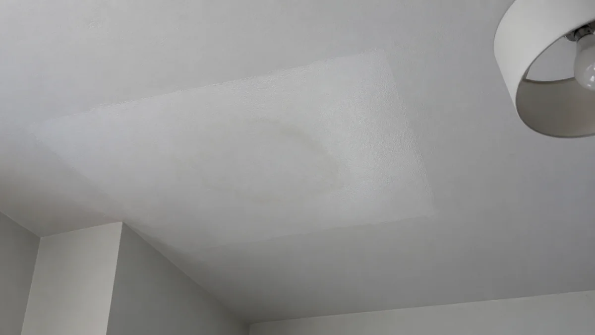 Plafond blanc repeint par un rectangle plus clair, au milieu duquel une auréole jaunâtre réapparaît