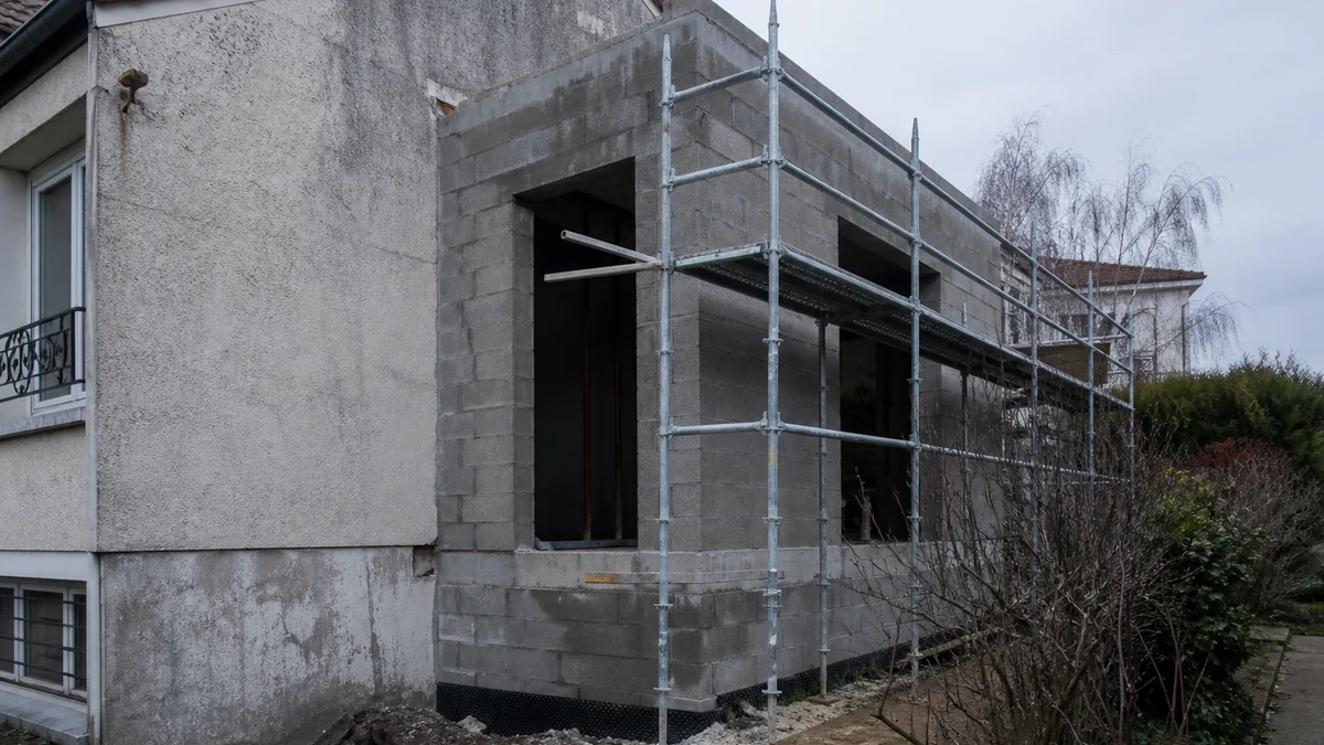 Extension en construction accolée à une maison ancienne, murs neufs en parpaings contre façade ancienne