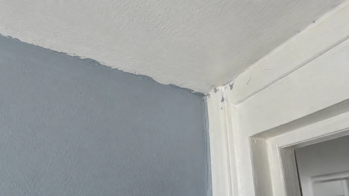 Angle entre un mur gris bleu, un plafond blanc et une huisserie : ligne de coupe ondulée, teinte débordant sur le plafond et coulures séchées sur le chambranle