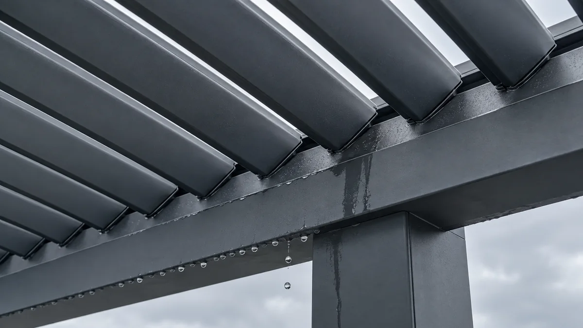 Dessous d'une pergola bioclimatique en aluminium anthracite : extrémités des lames au-dessus de la poutre-chéneau, rangée de gouttes sous la poutre et coulure le long du poteau