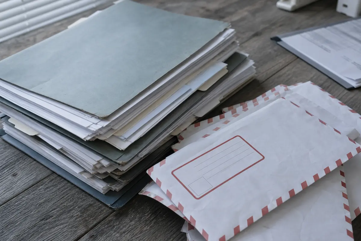 Pile de dossiers de chantier et d'enveloppes de courrier recommandé sur un bureau, étiquettes floutées, éclairage naturel froid