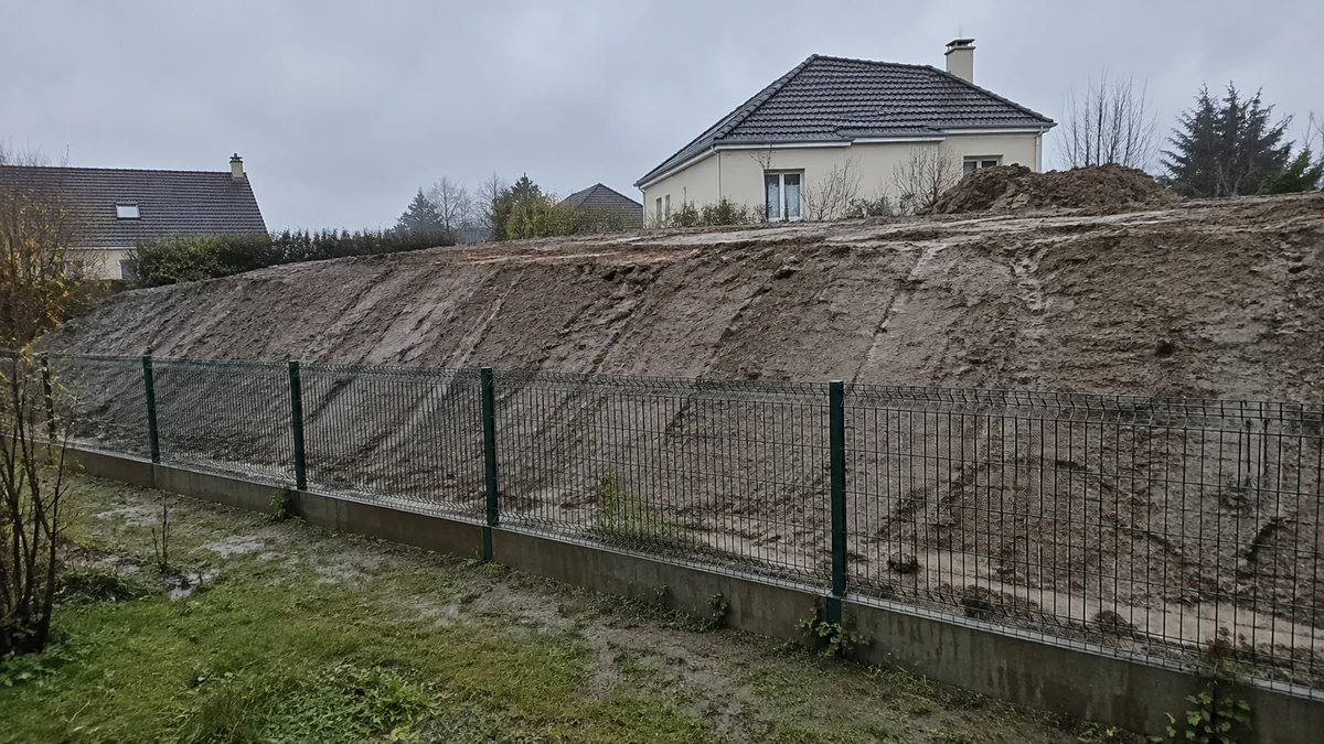 Remblai de terre récemment rapporté sur une parcelle voisine, surplombant une clôture de jardin