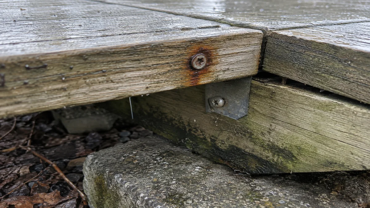 Gros plan sur une vis de fixation rouillée et une lambourde présentant des moisissures noirâtres au point de contact avec une dalle en béton