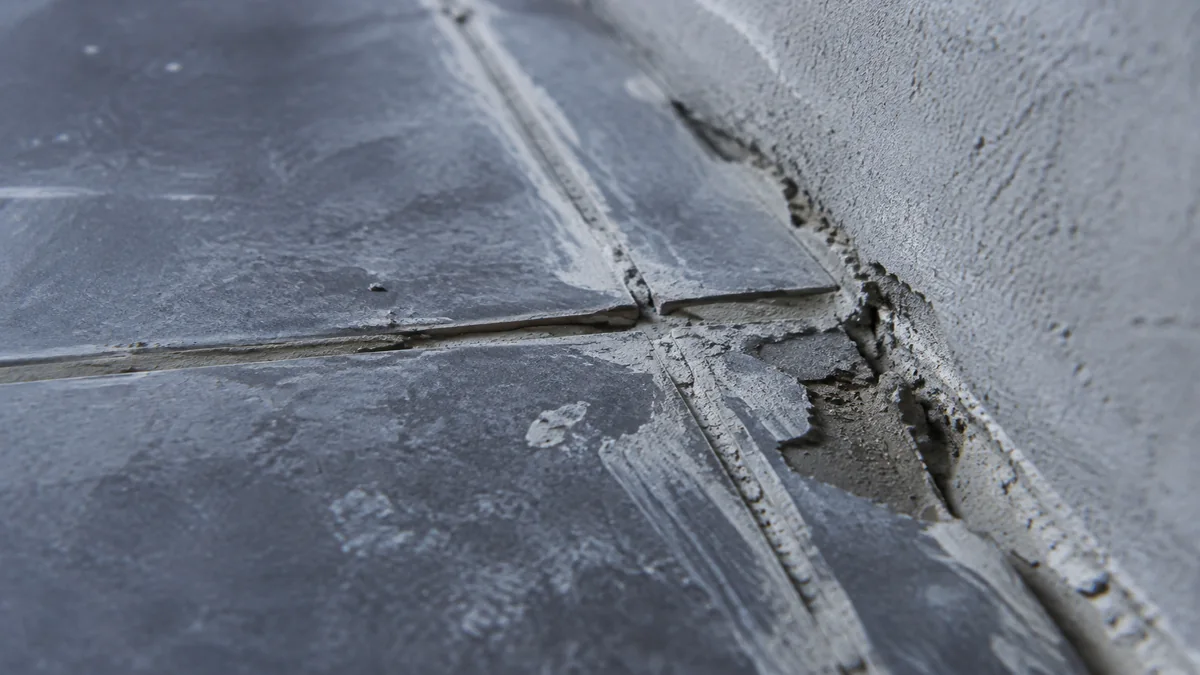 Angle de mur carrelé avec des joints irréguliers, du mortier débordant et une coupe de carreau mal ajustée