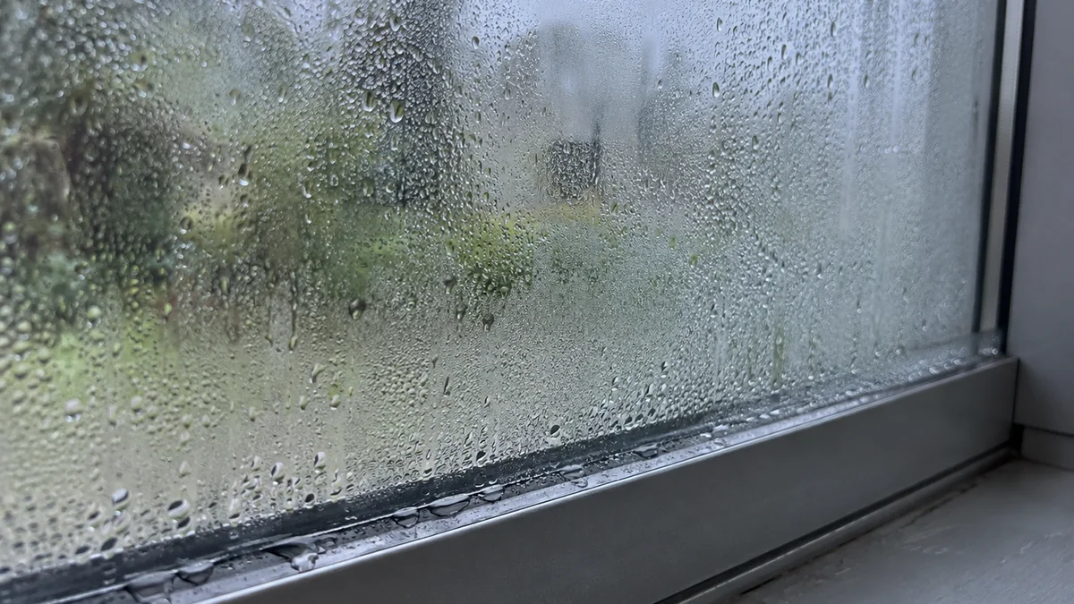 Vue intérieure d'une véranda montrant une forte condensation avec gouttes d'eau sur un grand panneau vitré et le bas du profilé aluminium