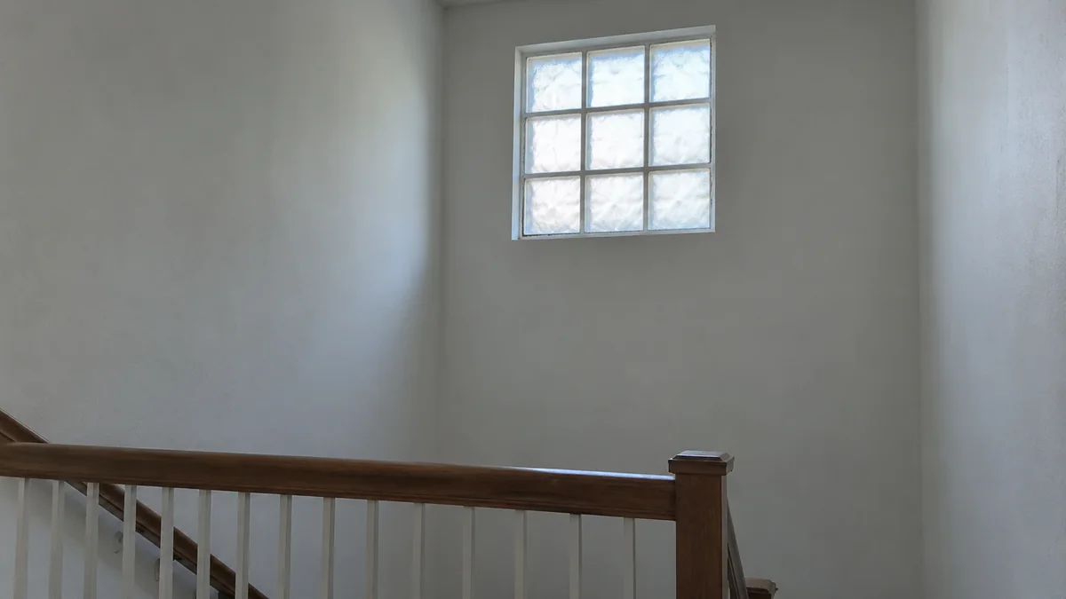 Cage d'escalier dont le mur est éclairé par un châssis carré de pavés de verre translucides placé haut au-dessus de la main courante, sans ouvrant