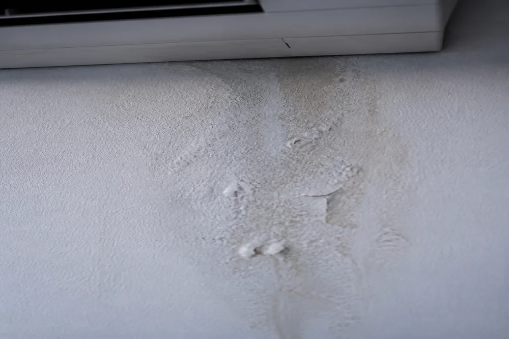 Tache d'humidité descendant sur un mur intérieur sous une unité de climatisation murale, signe d'un défaut d'évacuation des condensats