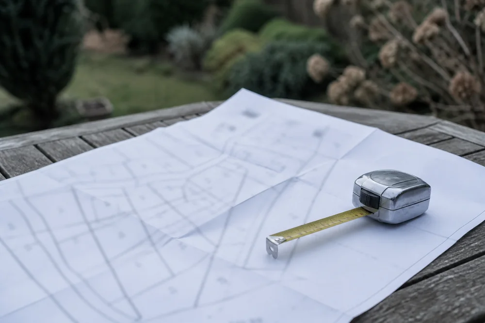 Plan cadastral déplié sur une table de chantier avec un mètre ruban de géomètre posé dessus